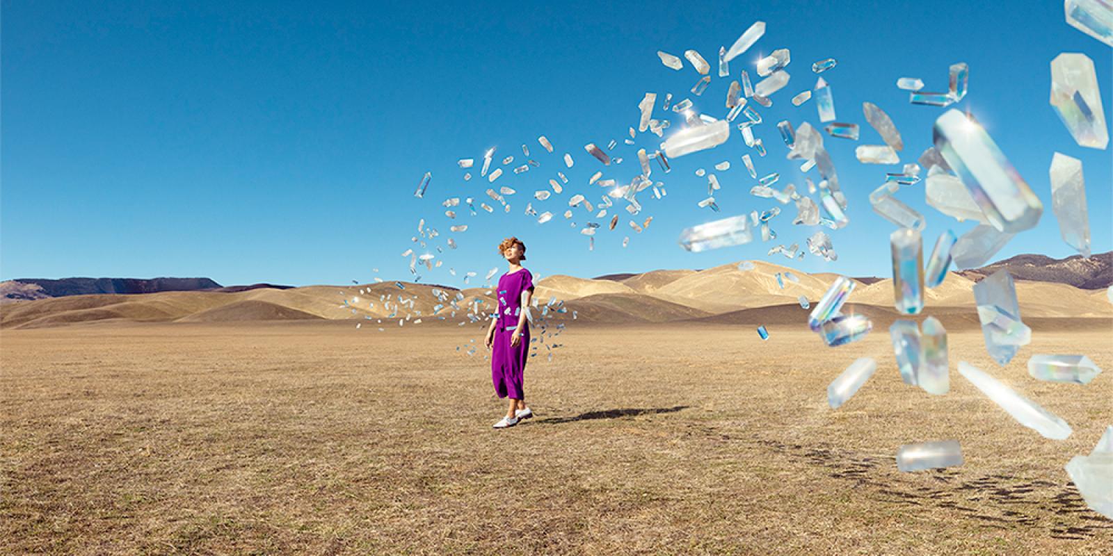 Image of a woman on a desert with crystals flying at her
