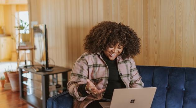 Girl smiling while sitting on couch while using a laptop