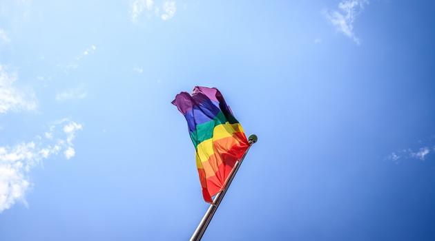 Pride Flag Waving in Wind with Blue Sky Background