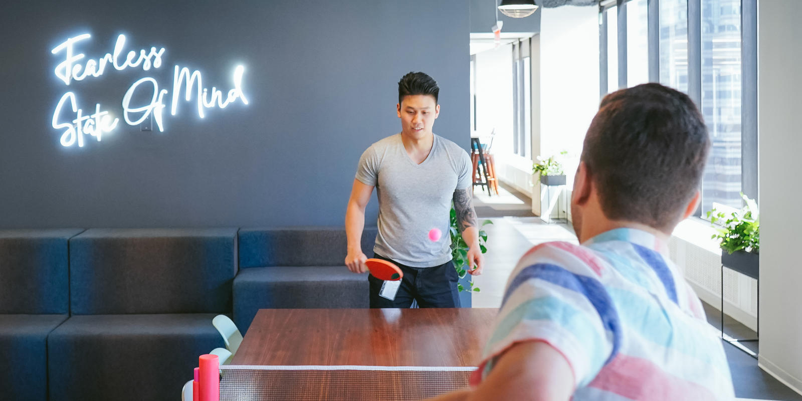 Zeno staff in New York playing ping pong in front of a wall that says Fearless State of Mind