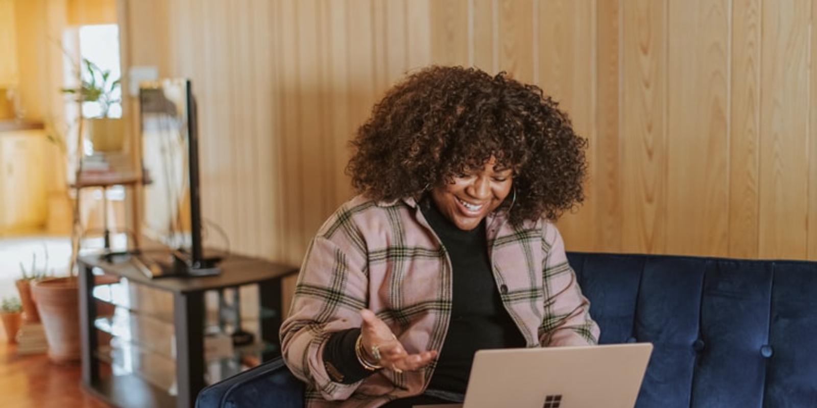 Girl smiling while sitting on couch while using a laptop