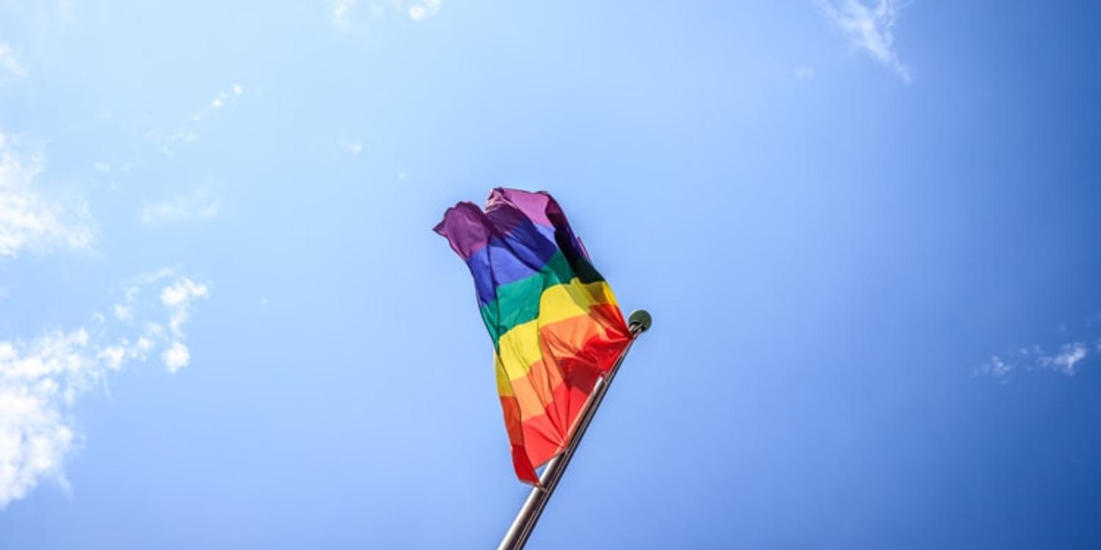 Pride Flag Waving in Wind with Blue Sky Background