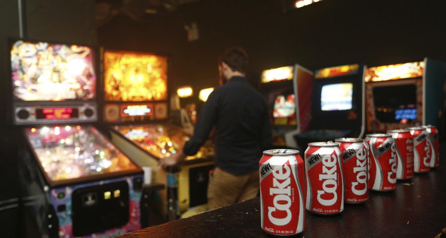 Bottles of Coke on Bar Table Next to Arcade Games Image